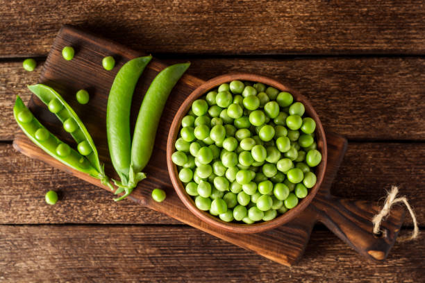 istock Fresh green peas in ceramic bowl on dark wooden background 831737230