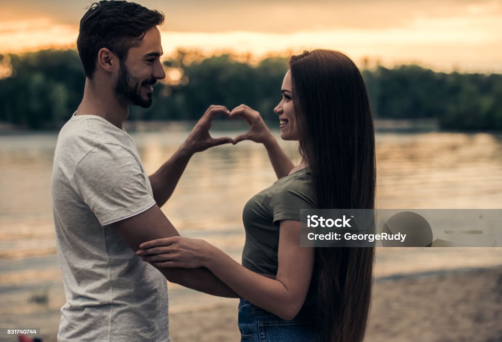 Romantic young couple Happy young couple is making heart and smiling while viewing sunset at the river Adult Stock Photo