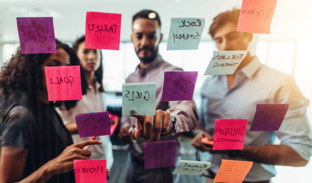 istock Business team looking at sticky notes posted  on glass wall in office. 831741106