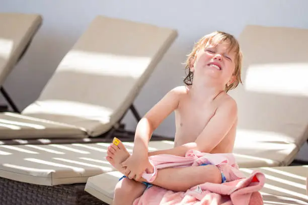 A boy have injured his leg and is crying and suffering pain sitting on a chaise lounge at the beach