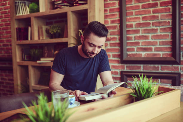 istock Young Handsome Man Reading Book in a Modern Cafe Restaurant 831752116