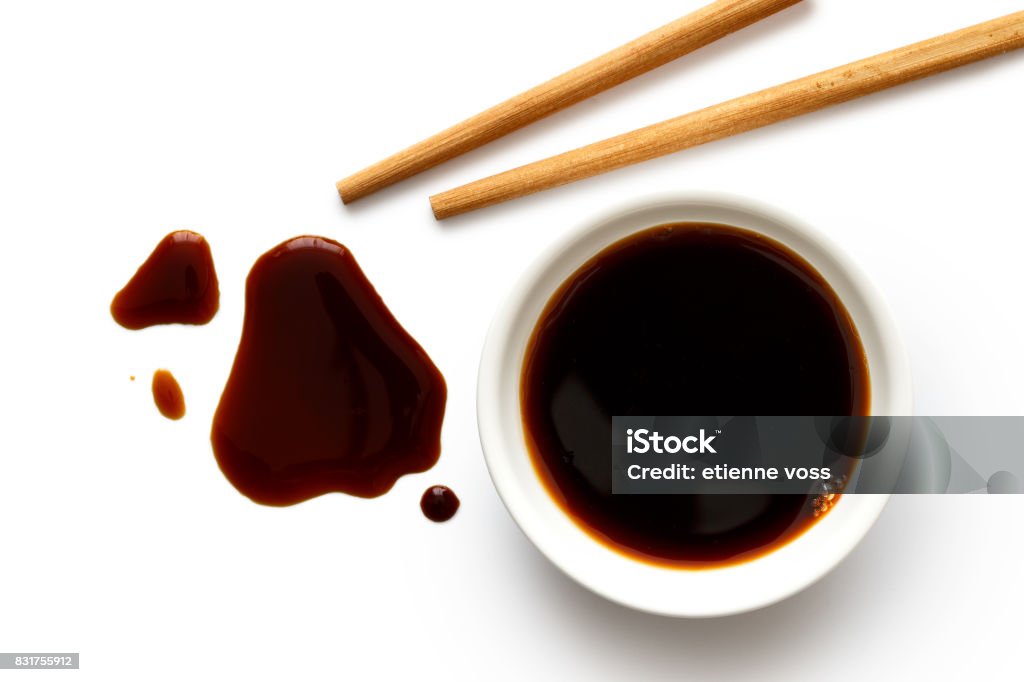 Soya sauce in white ceramic bowl on white from above with wooden chopsticks. Spilled soya sauce. Soy Sauce Stock Photo