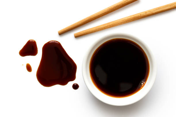 Soya sauce in white ceramic bowl on white from above with wooden chopsticks. Spilled soya sauce. Soya sauce in white ceramic bowl on white from above with wooden chopsticks. Spilled soya sauce. soy sauce photos stock pictures, royalty-free photos & images
