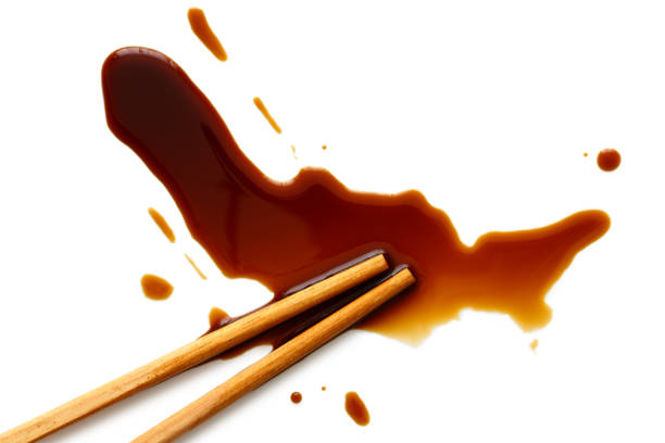 Spilled soya sauce on white with wooden chopsticks from above.