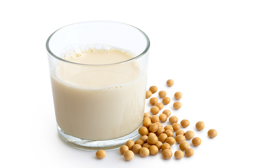 Glass of soya milk with froth isolated on white. Spilled soya beans.