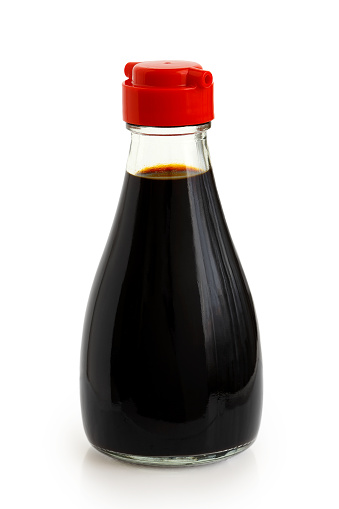 Glass bottle of soya sauce with red plastic lid isolated on white.