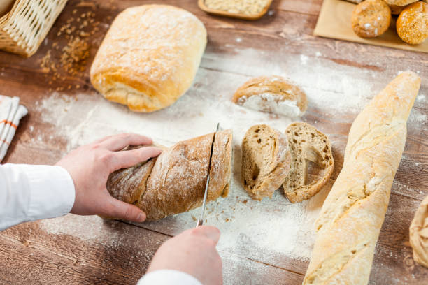 istock Male hands cutting fresh bread on the wooden table, selective focus 831796998