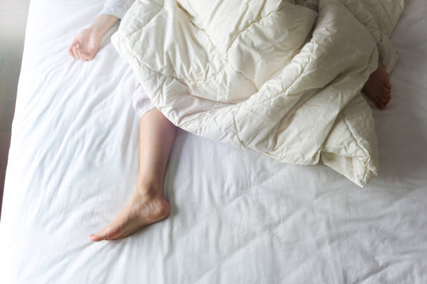 pies desnudos de una mujer joven en cama blanca - sheet sleeping women bed fotografías e imágenes de stock