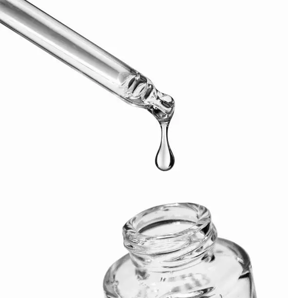 Photo of Drop falls from a pipette into a cosmetic bottle on white background