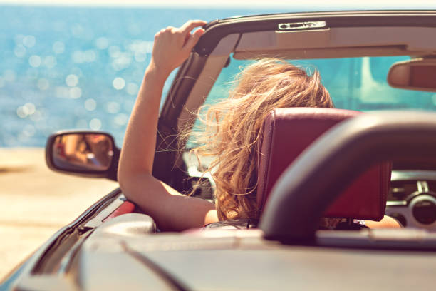 istock Beautiful blond smiling young woman in convertible top automobile looking sideways while parked near ocean waterfront 831837194