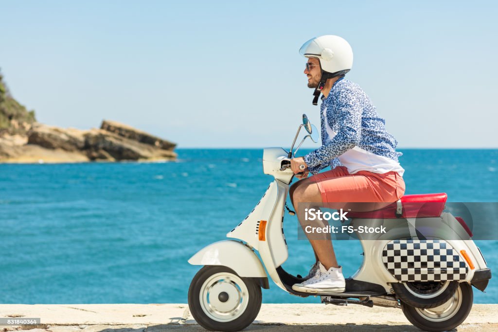 Handsome man posing on a scooter in a vacation context. Street fashion and style. Handsome man posing on a scooter in a vacation context. Street fashion and style Motorcycle Stock Photo