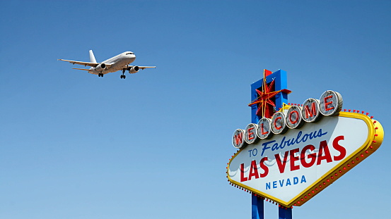 The iconic Welcome to Las Vegas sign is shown with a low flying airplane approaching the airport.  This conceptual image illustrates how people arrive in and are welcomed to Las Vegas, Nevada.