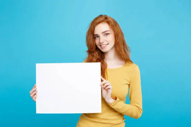 Business Concept - Close up Portrait young beautiful attractive redhair girl smiling showing blank sign. Blue Pastel Background.