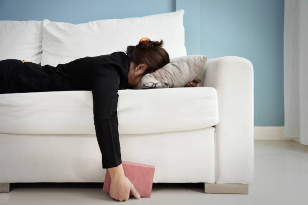 Tired Asian Business woman. Exhausted, Tired Asian Business woman in black shirt holding notebook and sleeping on white sofa with blue wall. Stress from overtime working concept. exhaustion stock pictures, royalty-free photos & images