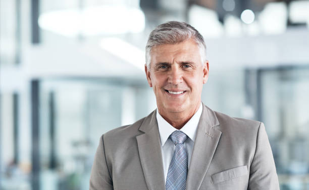 Confidence got him to the top Shot of a confident mature businessman standing in a modern office headshot stock pictures, royalty-free photos & images
