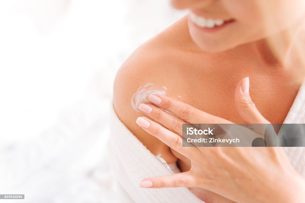 Close up of female fingers that applying lotion Nourishing cream. Delighted woman keeping smile on her face and turning head while expressing positivity Moisturizer Stock Photo