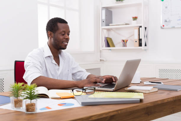 istock Young black businessman working with laptop in modern white office 831970888
