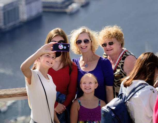 Family enjoying the view from top of Mount Fløyen. Bergen city Bergen, Norway - August 9, 2017: Family enjoying the view from top of Mount Fløyen taking selfie. Bergen city including seen in background. Cruising ships in port. fløyen stock pictures, royalty-free photos & images