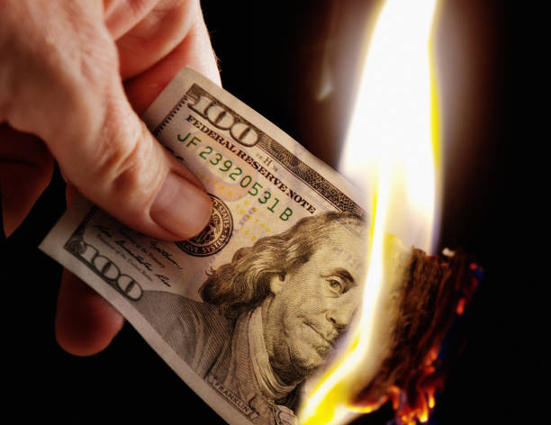 mano tiene bruciando la bolletta americana da cento dollari - money down the drain foto e immagini stock
