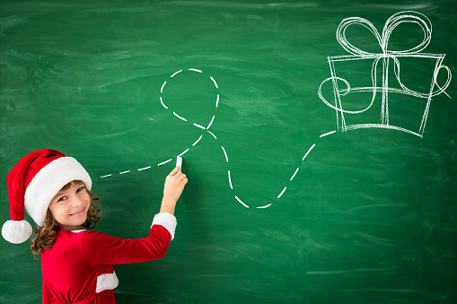 Happy child wearing Santa Claus draws on green blackboard. Christmas Xmas Winter Holiday Concept