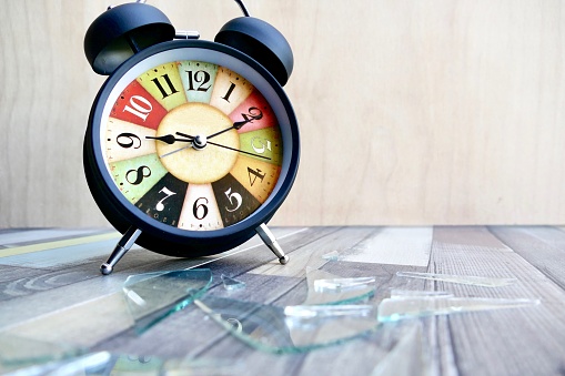 Damaged vintage colorful alarm clock, glass lying on wooden floor
