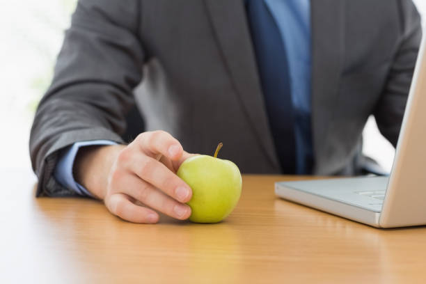 istock Smartly dressed businessman with laptop and apple at office 832071940