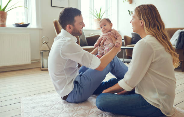 Smiling young parents sitting with their baby girl at home Smiling young mother and father sitting on their living room floor together at home cradling their adorable baby daughter lifestyle newborn stock pictures, royalty-free photos & images