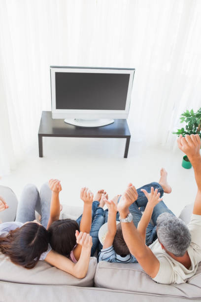 istock Family sitting on sofa cheering in front of television 832080830