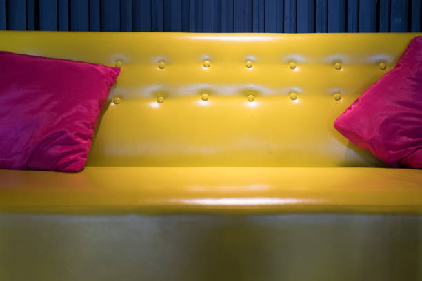 yellow leather sofa with pink fabric pillow beside black wall