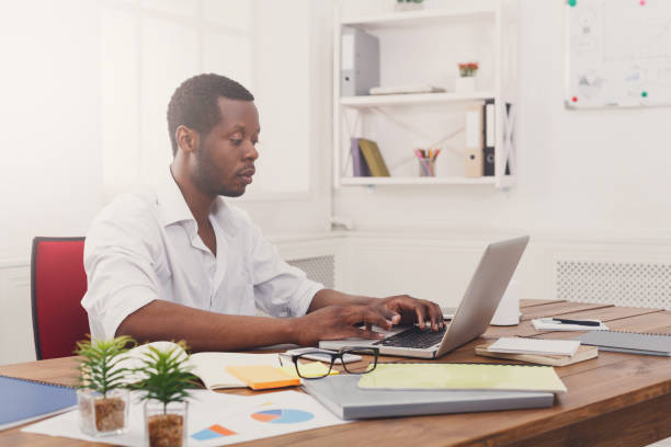 istock Young black businessman working with laptop in modern white office 832089566
