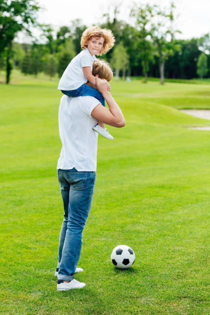 istock father carrying little son on shoulders while standing with soccer ball 832093336