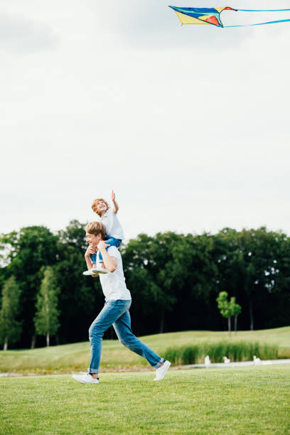 istock happy father carrying little son on shoulders while playing with kite at park 832096606