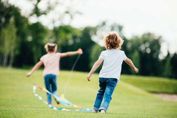 vue arrière du mignon petit garçon et fille jouant avec lite dans le parc - back lite photos et images de collection