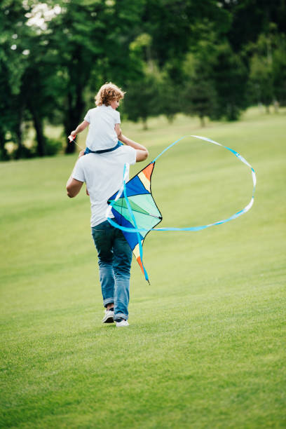 istock back view of father carrying little son on shoulders while playing with kite at park 832099828