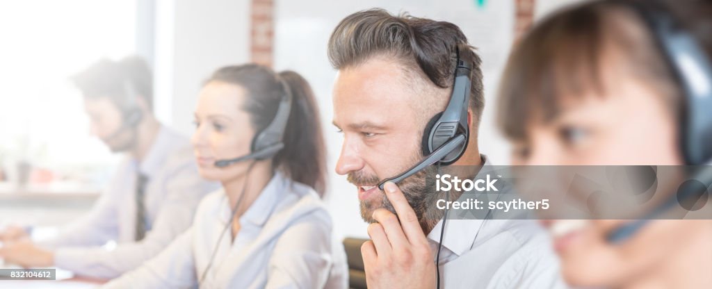 Call center worker accompanied by his team. Call center worker accompanied by his team. Smiling customer support operator at work. Young employee working with a headset. Call Center Stock Photo