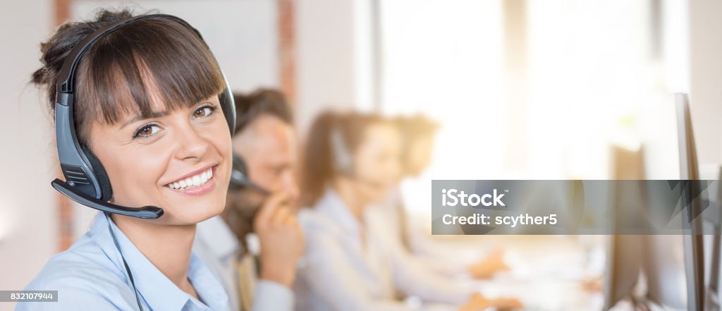 Call center worker accompanied by her team. Call center worker accompanied by her team. Smiling customer support operator at work. Young employee working with a headset. Call Center Stock Photo