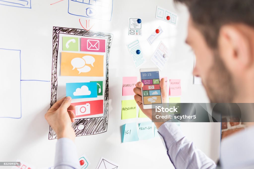 Designer drawing website ux app development. Designer man drawing website ux app development and holding smart phone on hand. User experience concept. Mobile App Stock Photo