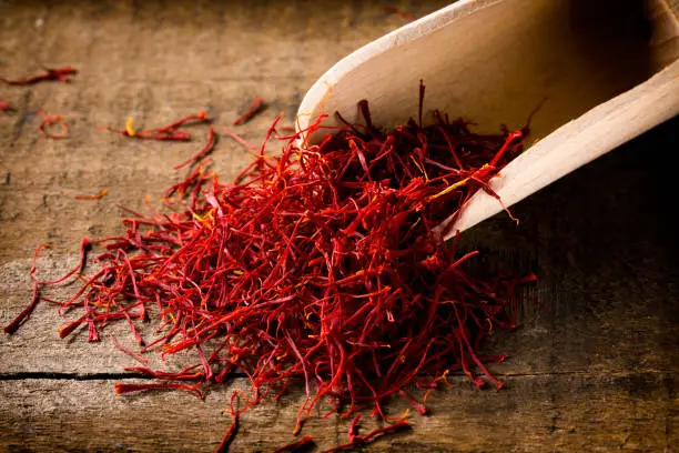 saffron threads with spice shovel on wooden background, closeup,