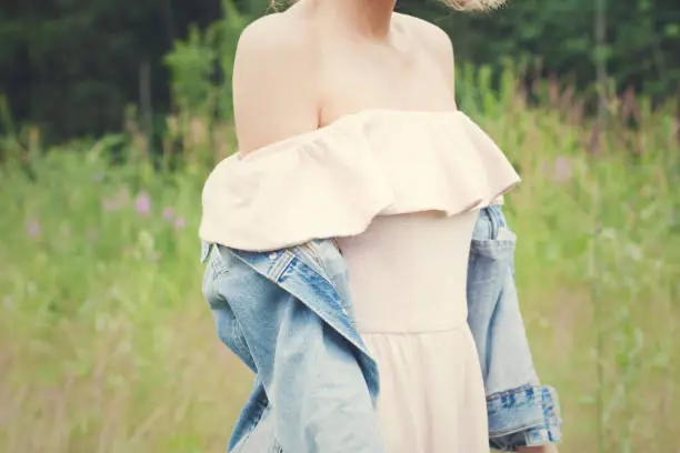 Girl dressed pale pink dress and denim jacket walking in park. Landscape background.