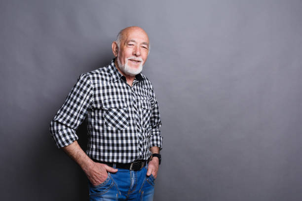 Serious senior man posing with hands on hips, gray studio background, copy space