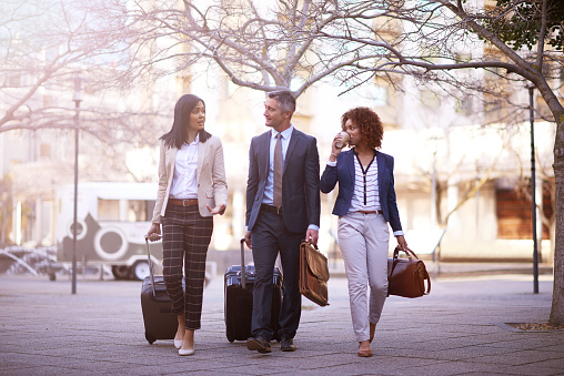 Shot of a group of business people walking and talking to each other while carrying their luggage outside