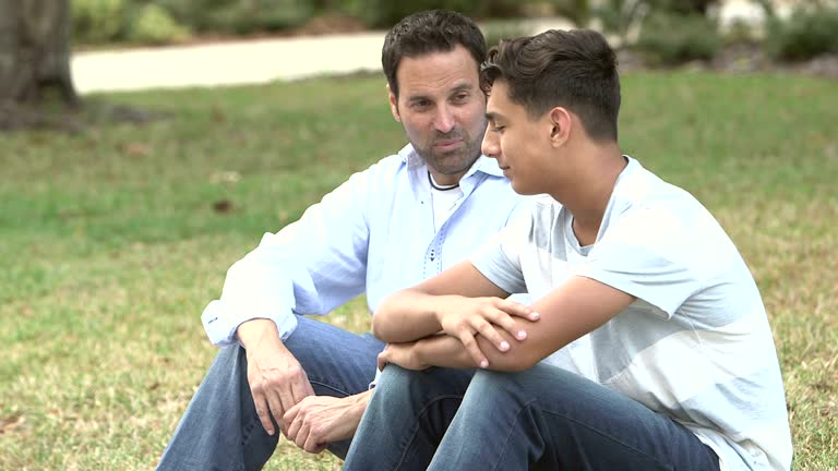 Father and son sitting on lawn, talking