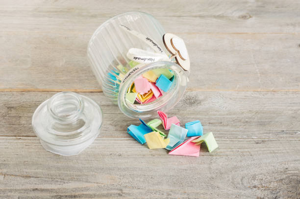 Glass jar with handmade wooden hearts decorations and ribbon filled with colorful pastel paper notes spilling over.