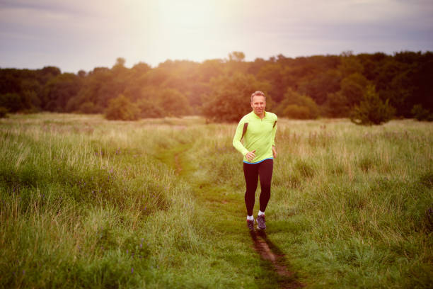 Fit muscular man jogging on a rural trail at sunset through grassland wearing sportswear in an active lifestyle concept