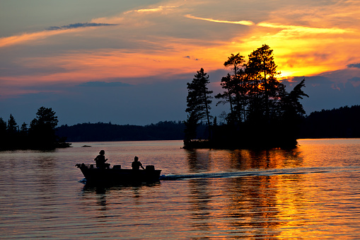 Fisherman fishing on a small boat at sunset over Burntside Lake, Ely Minnesota. Located in the Superior National Forest. Burntside Lake a popular tourist destination in the summer in Minnesota. Beautiful scenic area adjacent to the Boundary Water Canoe Area.