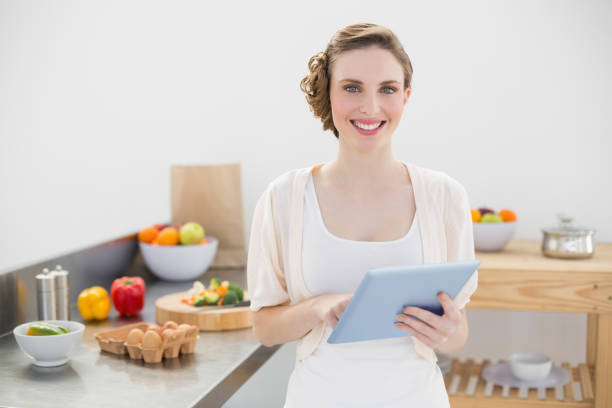 istock Cheerful lovely woman holding her tablet standing in her kitchen 832150524