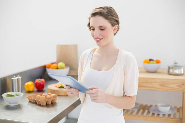 istock Smiling cute woman using her tablet standing in her kitchen 832150542