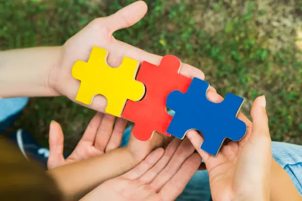 Close-up Of Hands Holding Three Colorful Jigsaw Puzzle Pieces