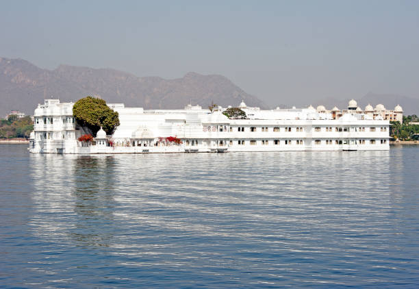 Lake Palace, Pichola Lake, Udaipur, Rajasthan, India. Lake Palace, Pichola Lake, Udaipur, Rajasthan, India. The famous royal Lake Palace seems to float in the centre of Lake Pichola, seen here from the lakeshore with the waters of the lake rippling in the foreground, Udaipur, Rajasthan, India lake palace stock pictures, royalty-free photos & images