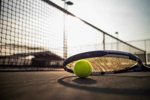 tennis ball and racket on hard court under sunlight - tennis court tennis ball racket imagens e fotografias de stock
